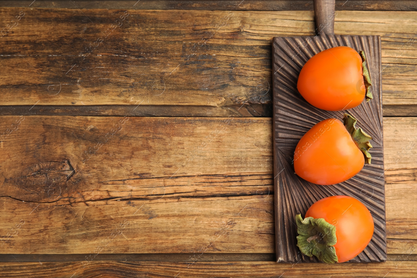 Photo of Tasty ripe persimmons on wooden table, top view. Space for text