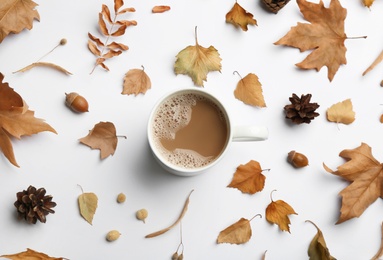 Cup of hot drink and autumn leaves on white background, flat lay. Cozy atmosphere