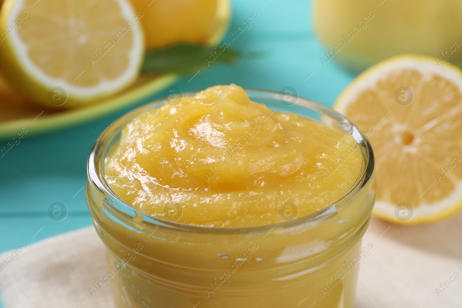 Photo of Delicious lemon curd in glass jar and fresh citrus fruit on table, closeup