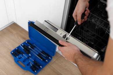 Serviceman repairing dishwasher door with screwdriver indoors, closeup