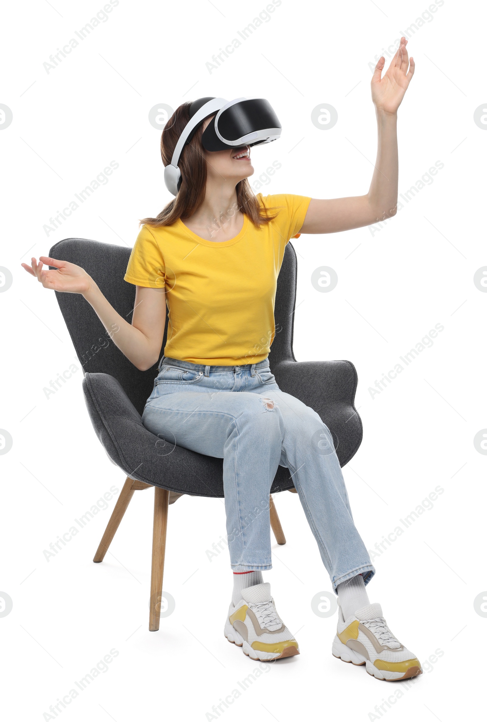 Photo of Smiling woman using virtual reality headset while sitting in armchair against white background