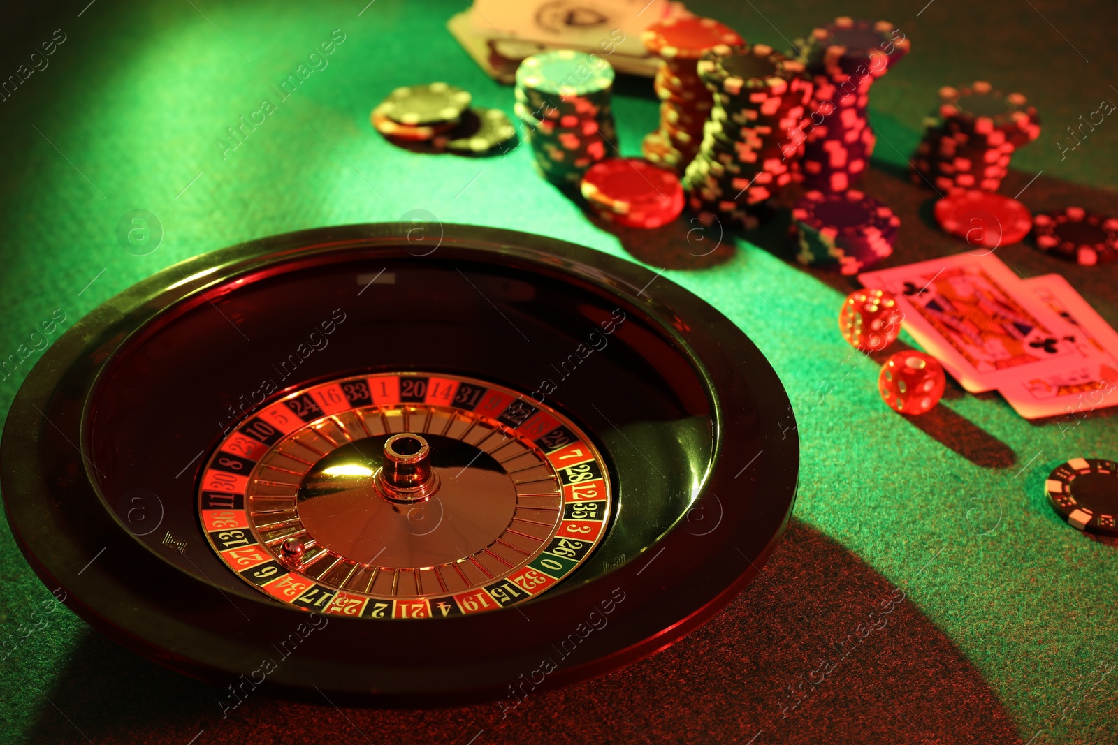 Photo of Roulette wheel with ball, playing cards and chips on green table. Casino game