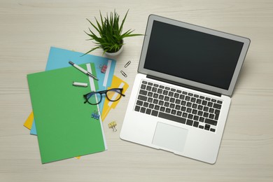 Modern laptop, glasses and office stationery on white wooden table, flat lay. Distance learning