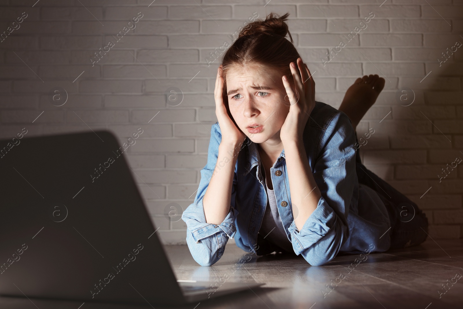 Photo of Shocked teenage girl with laptop on floor in dark room. Danger of internet