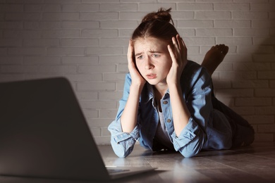 Shocked teenage girl with laptop on floor in dark room. Danger of internet