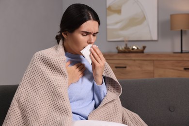 Photo of Woman coughing with tissue on sofa at home, space for text. Cold symptoms