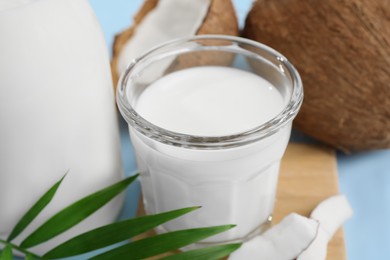 Photo of Glass of delicious vegan milk, coconuts and leaf on light blue background, closeup