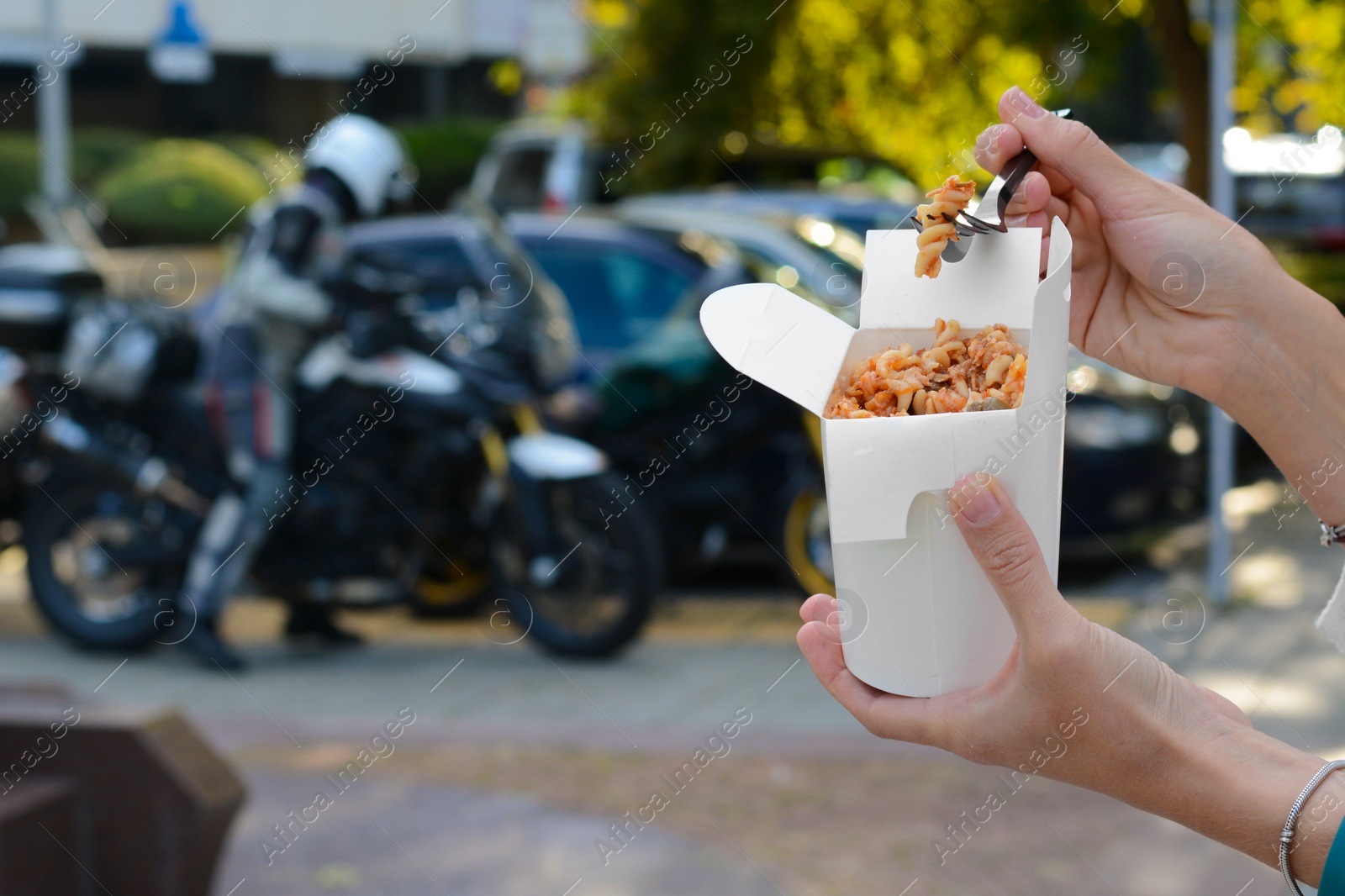 Photo of Woman eating takeaway noodles from paper box with fork outdoors, closeup and space for text. Street food
