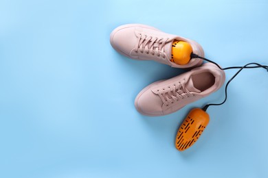 Photo of Pair of stylish shoes with modern electric footwear dryer on light blue background, top view. Space for text