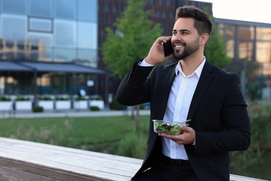 Photo of Smiling businessman talking by smartphone during lunch outdoors. Space for text