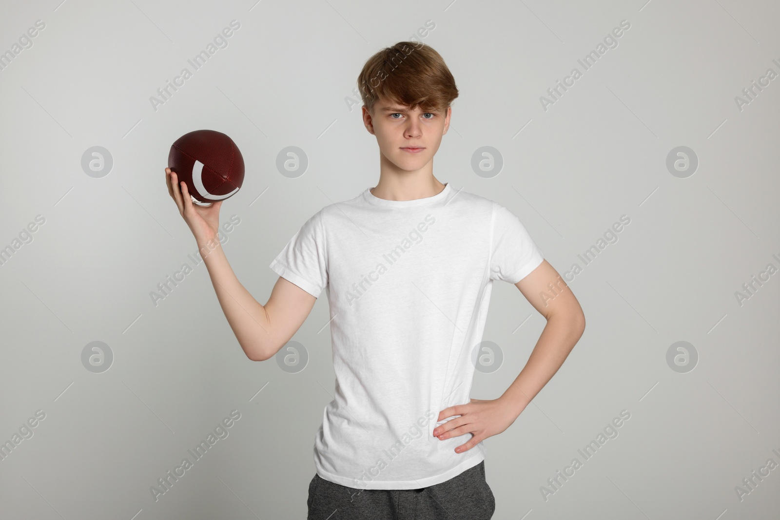 Photo of Teenage boy with american football ball on light grey background