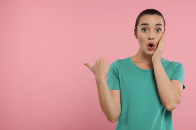 Photo of Special promotion. Surprised woman pointing at something on pink background. Space for text