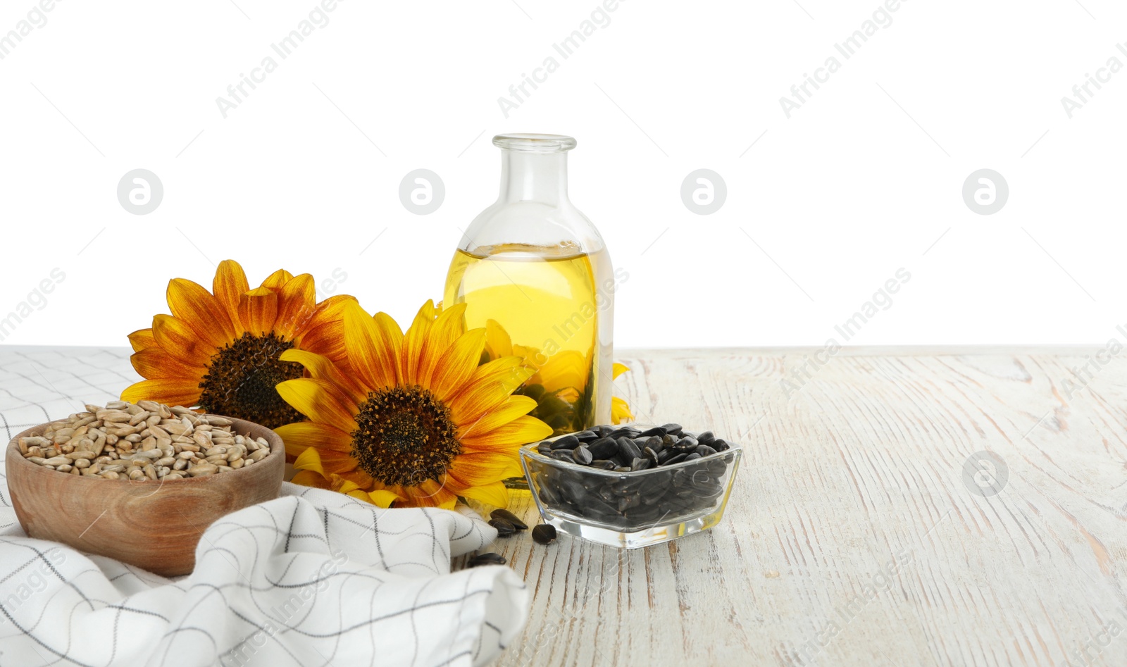 Photo of Sunflowers, bottle of oil and seeds on wooden table against white background, space for text