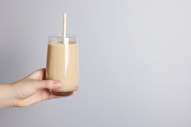 Photo of Woman holding glass of tasty smoothie on light grey background, closeup. Space for text