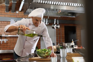 Photo of Professional chef pouring oil into bowl with fresh salad in restaurant kitchen, space for text