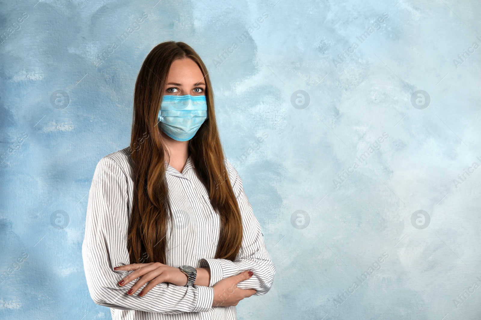 Photo of Woman with disposable mask on face against light blue background. Space for text