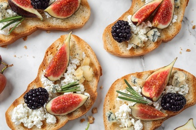 Bruschettas with cheese, figs and blackberries on white table, top view