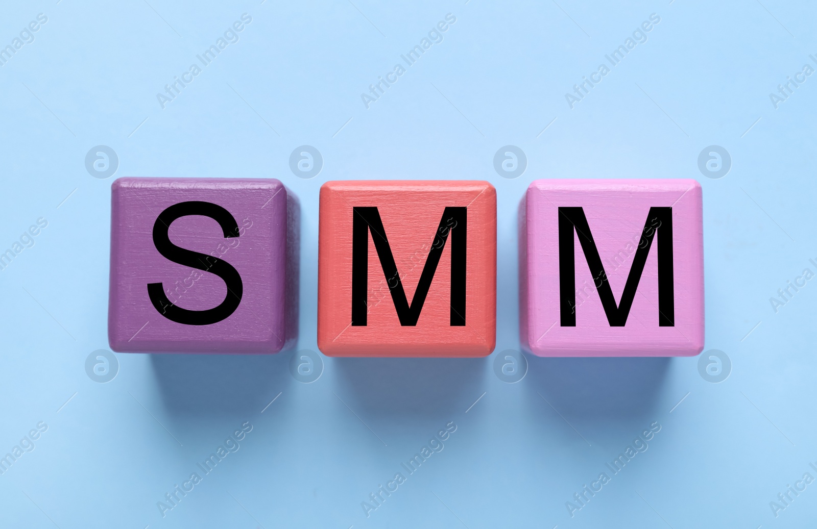 Photo of Colorful cubes with abbreviation SMM (Social media marketing) on light blue background, flat lay