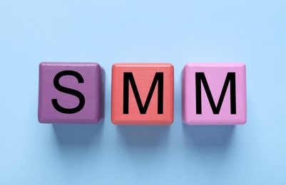 Photo of Colorful cubes with abbreviation SMM (Social media marketing) on light blue background, flat lay