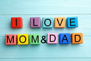 Photo of Words I LOVE MOM and DAD made from alphabet cubes on blue wooden table, flat lay