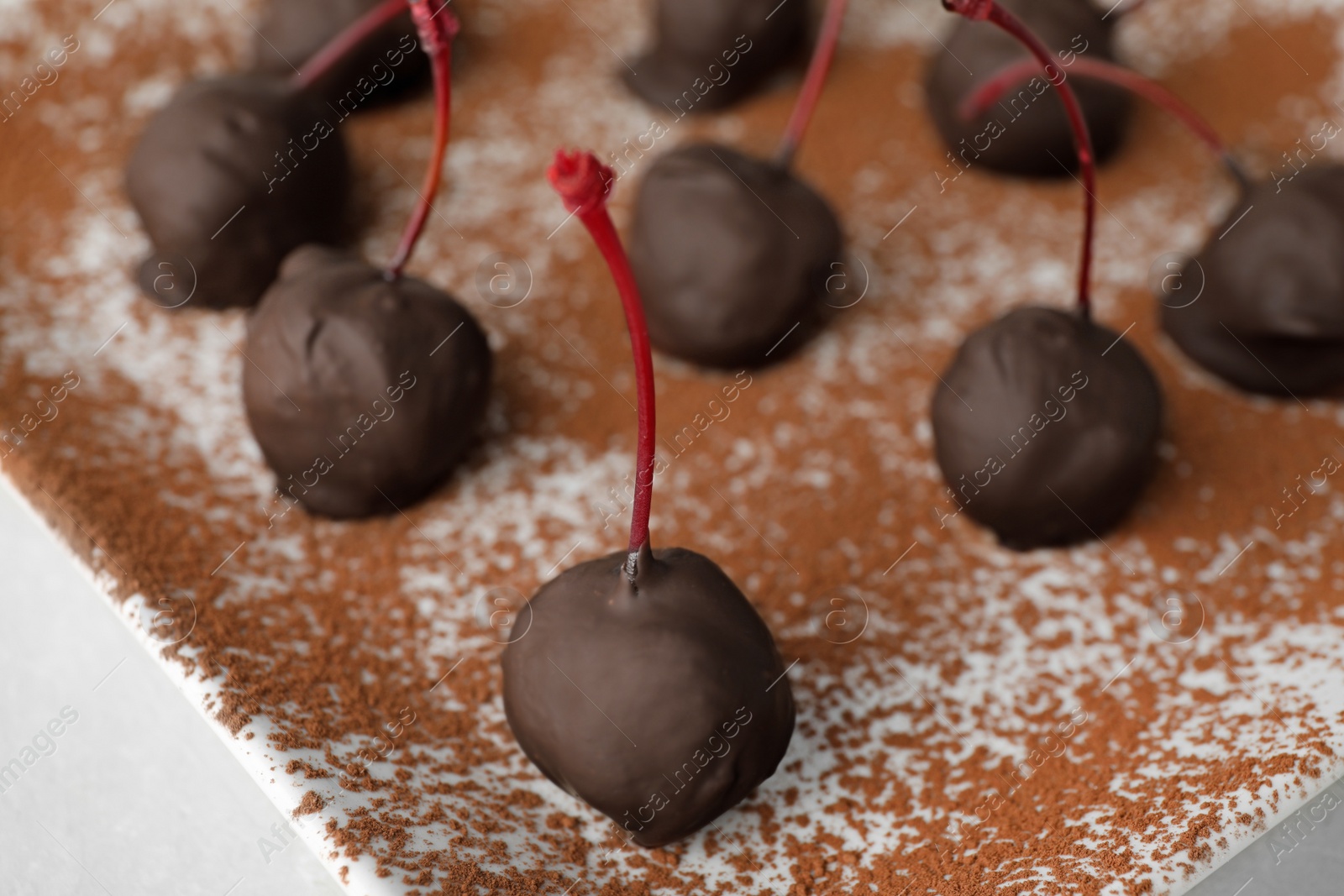 Photo of Chocolate dipped cherries on plate sprinkled with cocoa powder, closeup