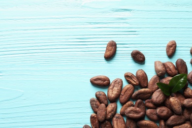 Tasty cocoa beans on blue wooden table, top view. Space for text