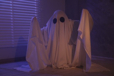 Photo of Creepy ghost. Woman covered with sheet near window in color lights