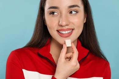 Happy young woman with bubble gum on light blue background
