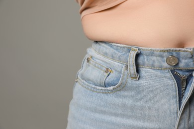 Photo of Overweight woman in tight jeans on grey background, closeup. Space for text