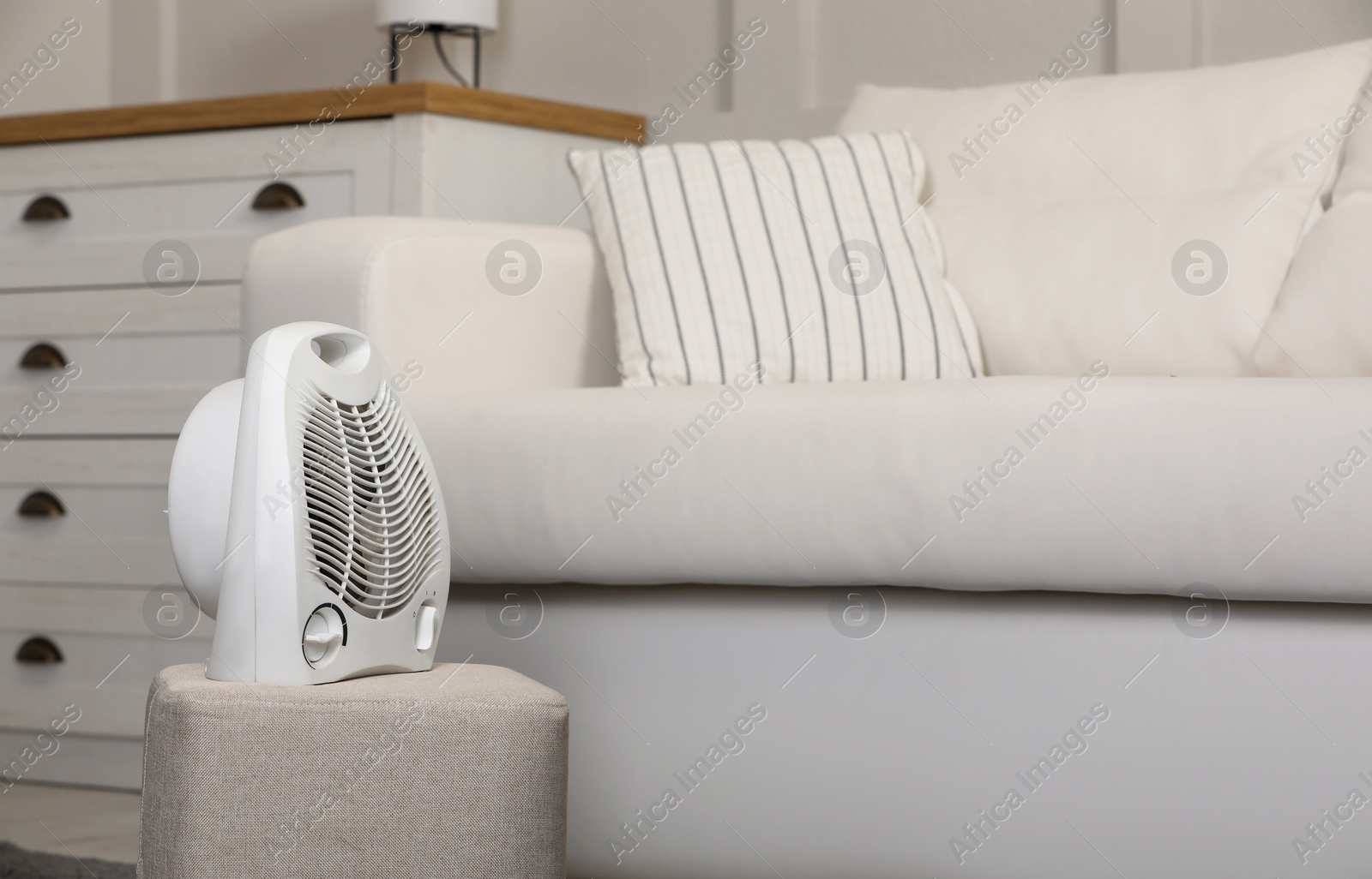 Photo of Electric fan heater on pouf in living room