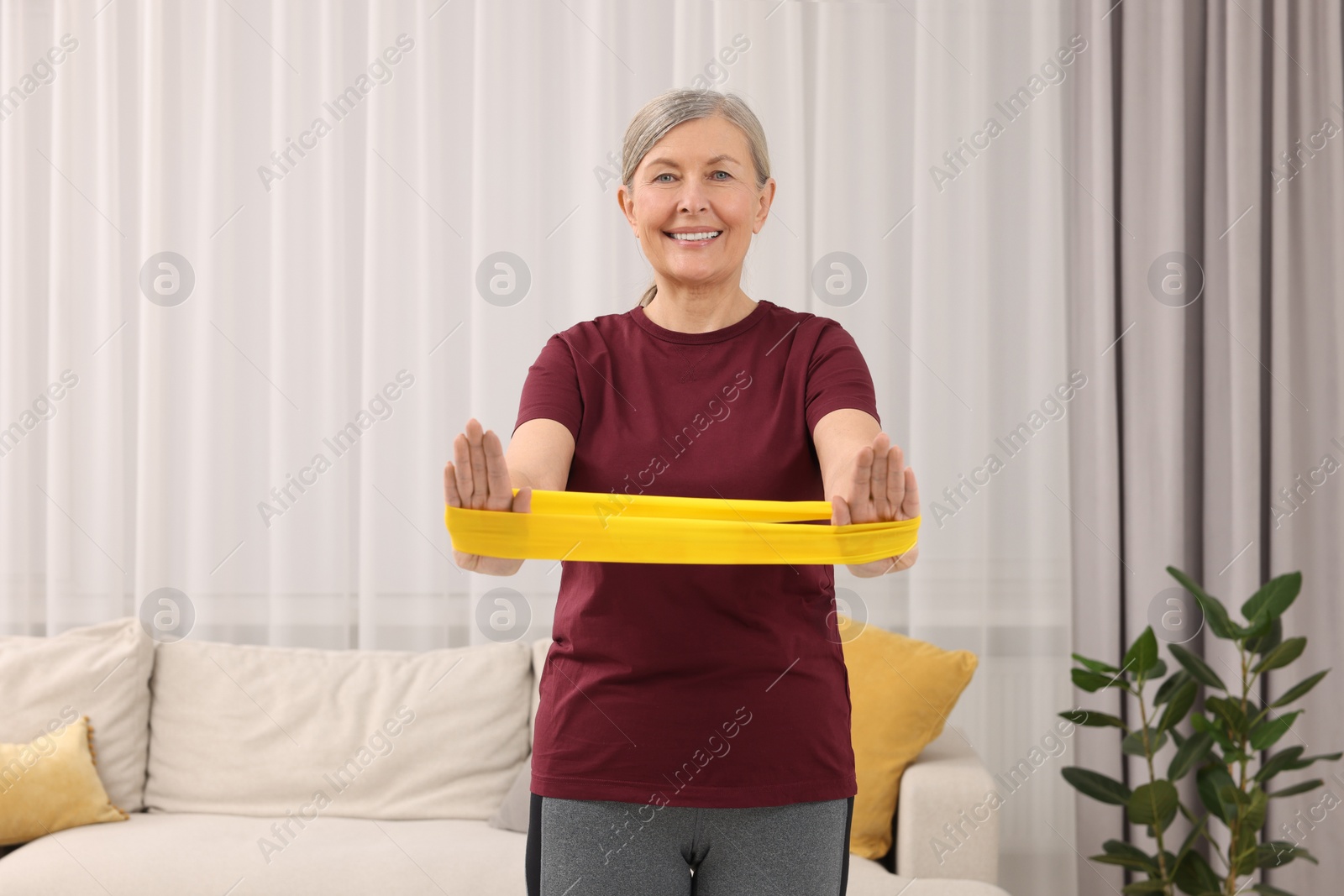 Photo of Senior woman doing exercise with fitness elastic band at home