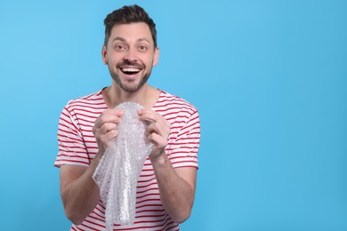 Happy man popping bubble wrap on light blue background, space for text. Stress relief