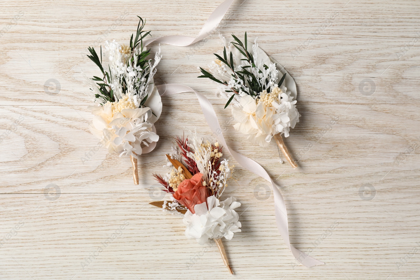 Photo of Stylish boutonnieres on white wooden table, flat lay