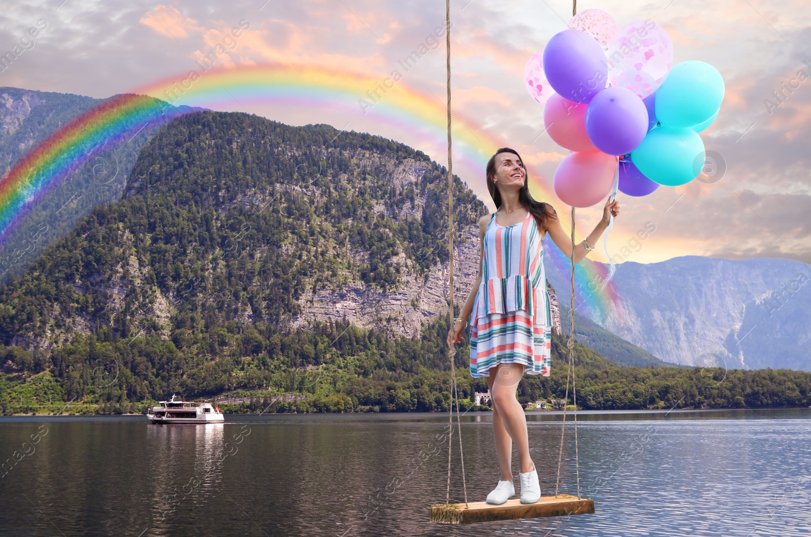 Image of Dream world. Young woman with bright balloons swinging, mountains and lake on background