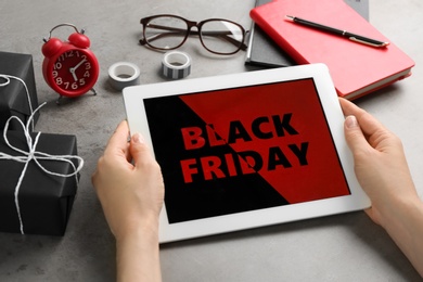 Photo of Woman using tablet with Black Friday announcement at grey table, closeup