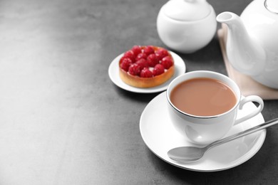 Photo of Delicious tea with milk in white cup near dessert on grey table. Space for text