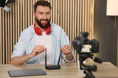 Photo of Smiling technology blogger with camera recording video review about WI-FI router at home