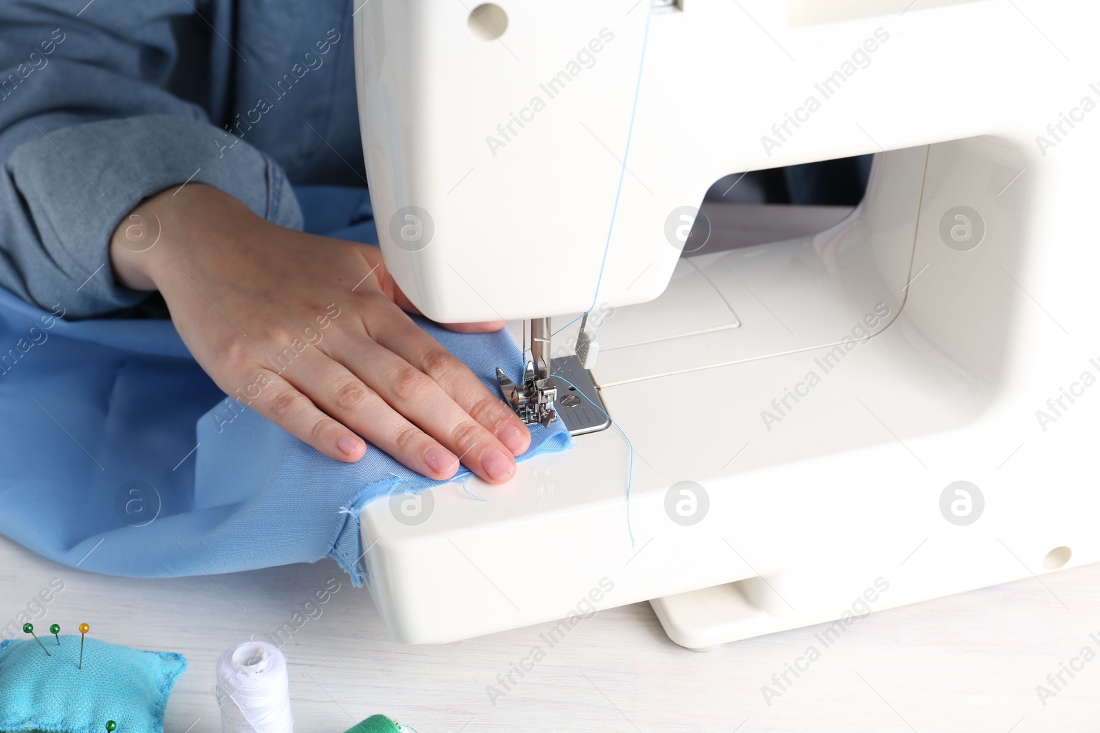 Photo of Seamstress working with sewing machine at white wooden table indoors, closeup