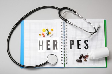 Notebook with word Herpes, different pills and stethoscope on grey background, flat lay