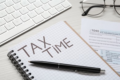 Photo of Notebook with words Tax Time, documents, keyboard and glasses on white wooden table