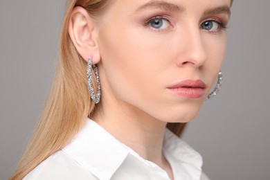 Photo of Beautiful young woman with elegant earrings on gray background, closeup