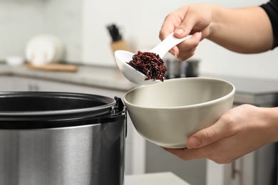 Photo of Woman putting brown rice into bowl from multi cooker in kitchen, closeup