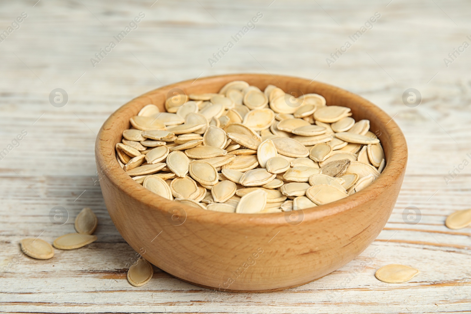 Photo of Bowl of raw pumpkin seeds on white wooden table