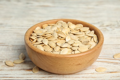 Photo of Bowl of raw pumpkin seeds on white wooden table