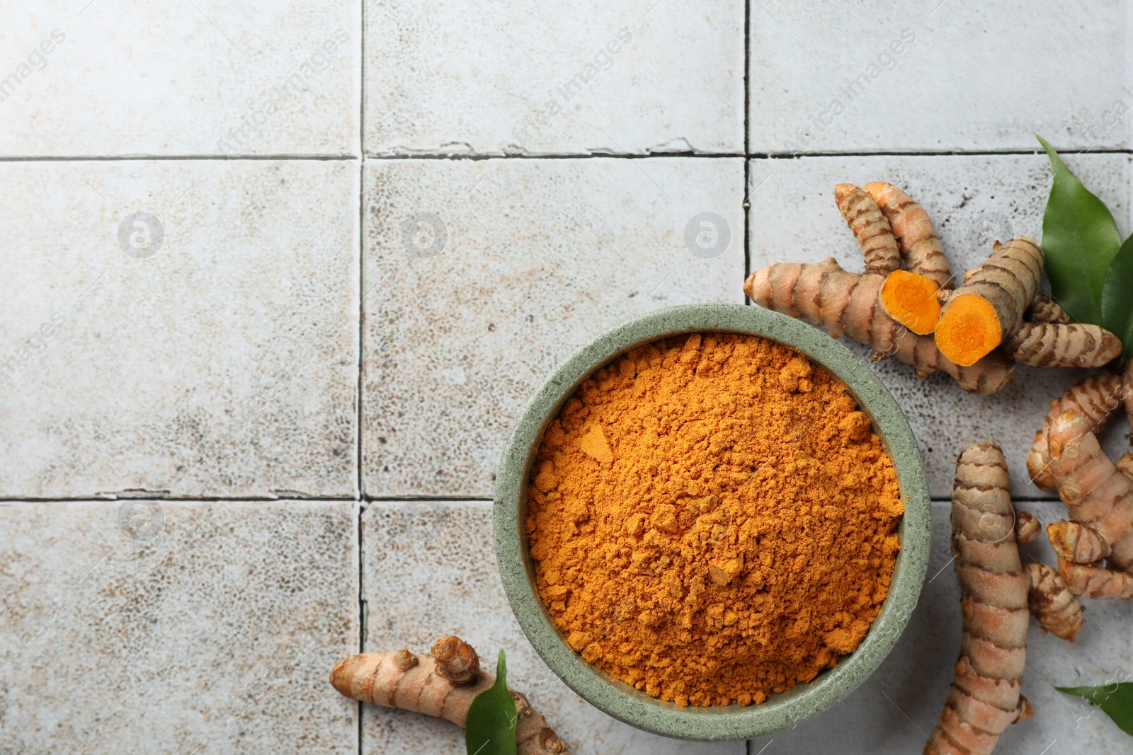 Photo of Aromatic turmeric powder, raw roots and leaves on light tiled table, flat lay. Space for text