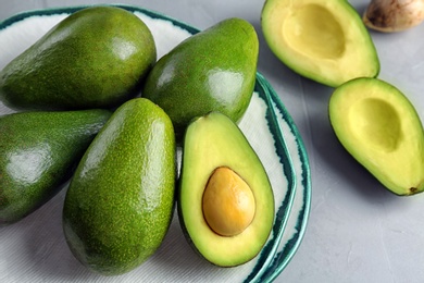 Plate with ripe avocados on grey table