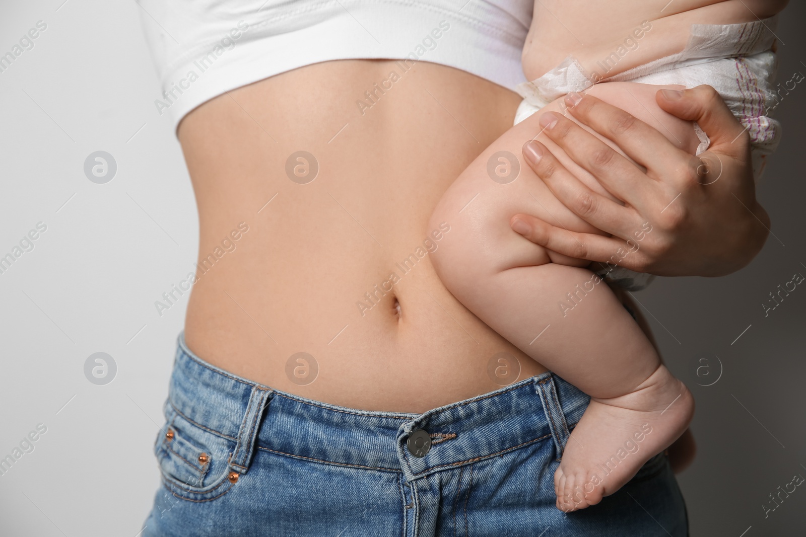 Photo of Mother with bare belly holding her baby on light grey background, closeup