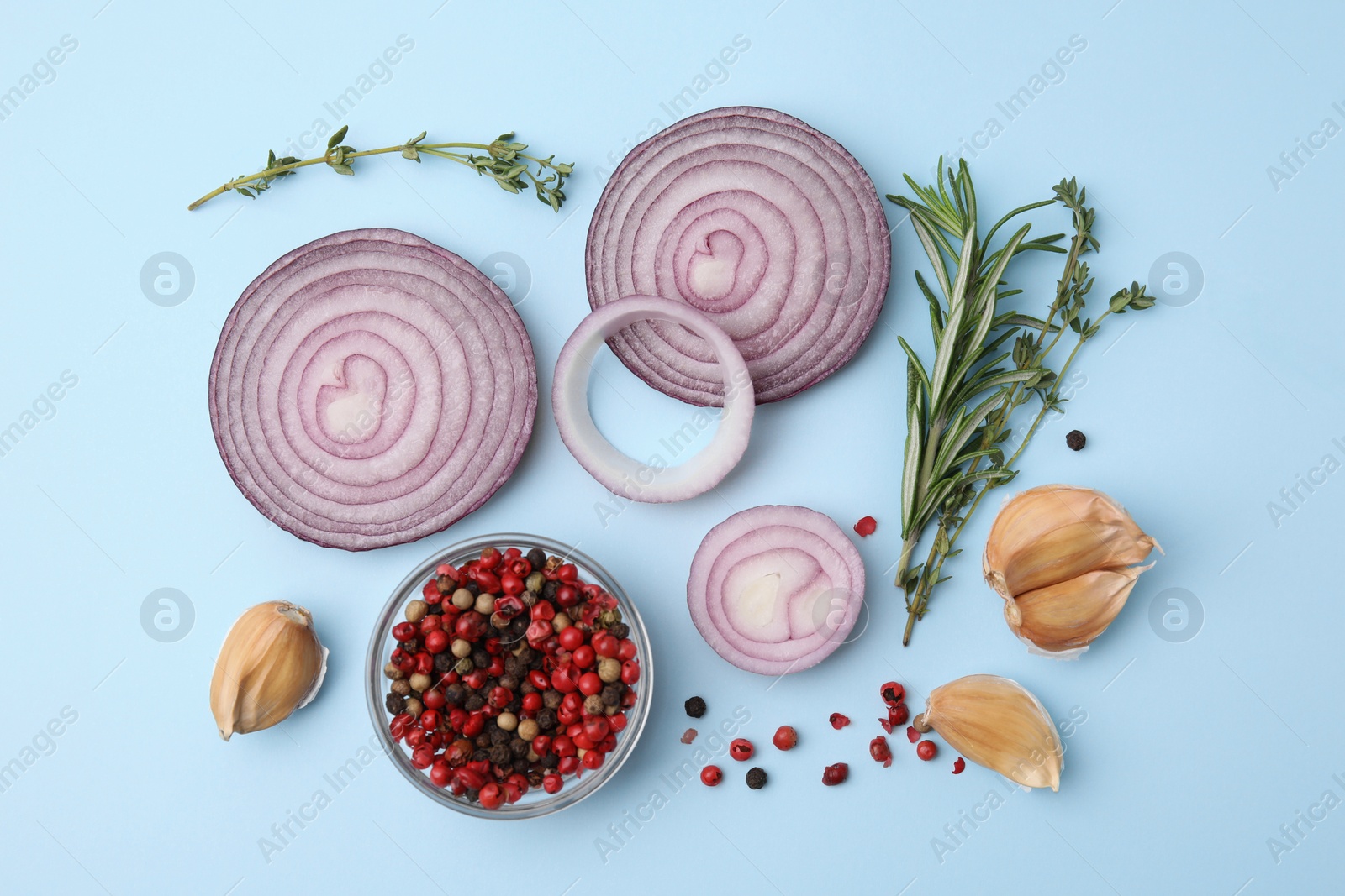 Photo of Fresh red onions, garlic, different herbs and spices on light blue background, flat lay