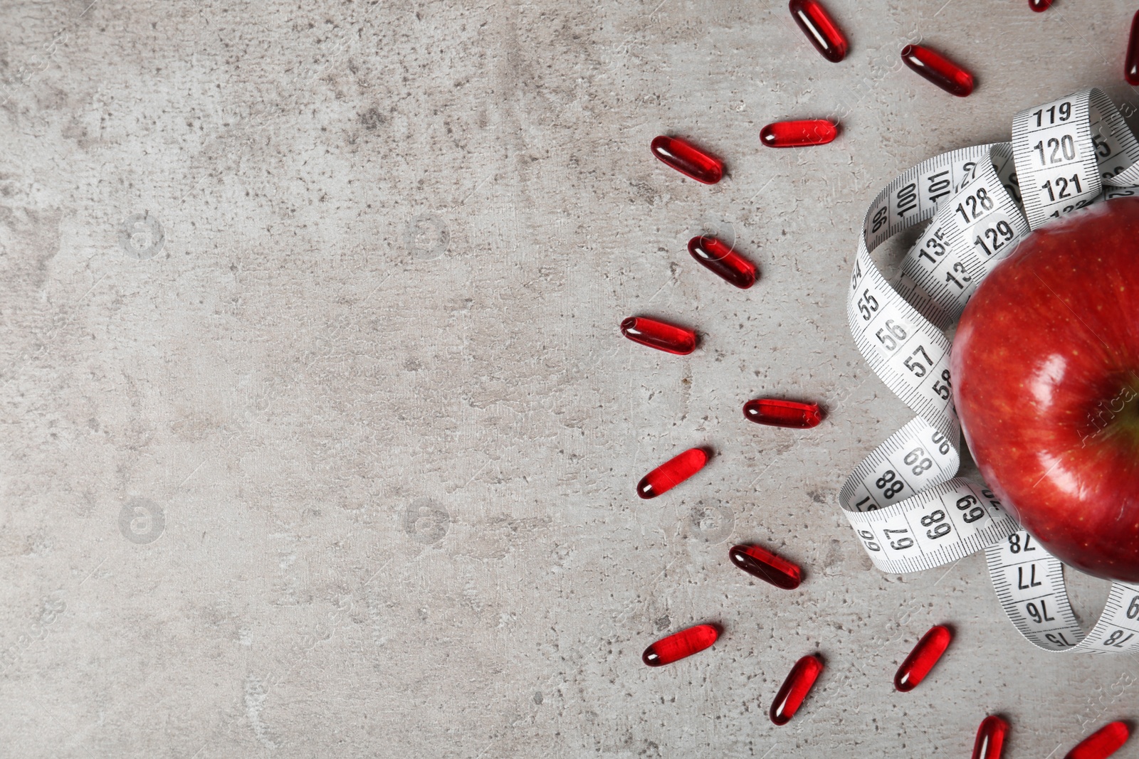 Photo of Weight loss pills with apple and measuring tape on grey background, flat lay. Space for text