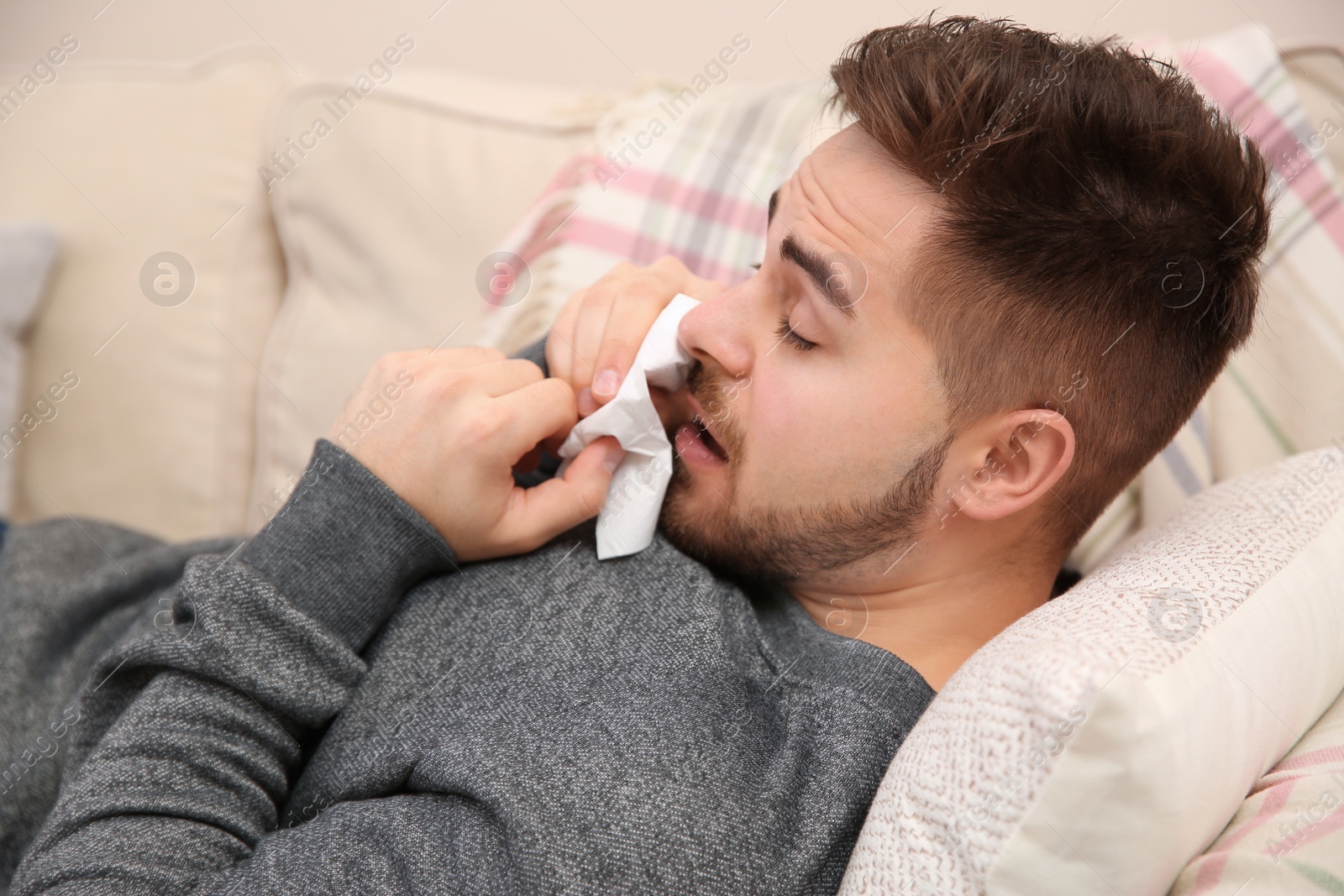 Photo of Sick young man sneezing at home. Influenza virus